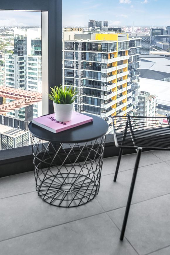 Balcony with round black table, potted plant, and chair overlooking city buildings