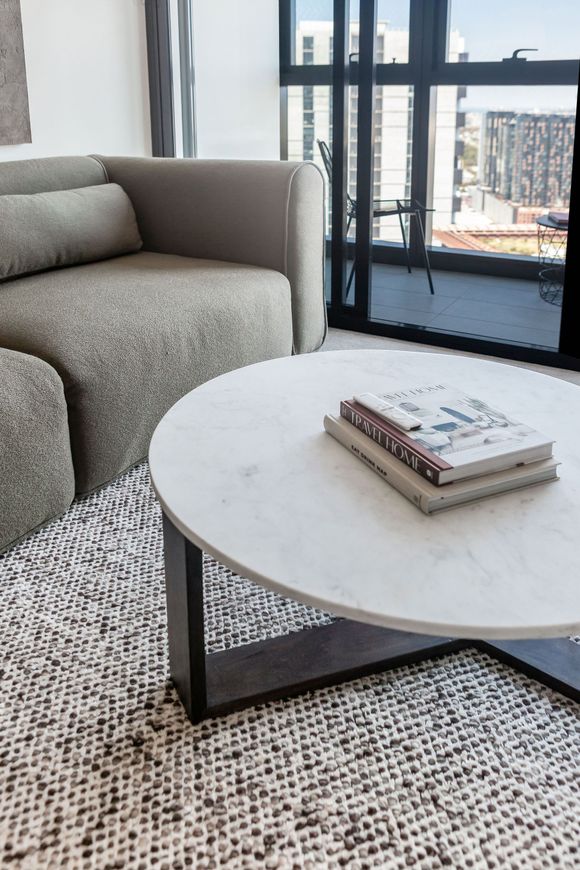 Modern living room corner with gray sofa, round white coffee table, and city view through large windows
