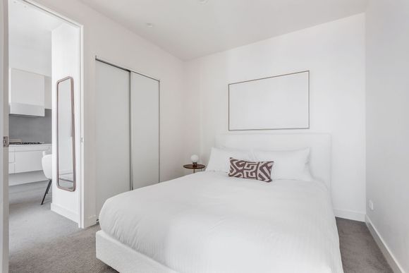 Bright white bedroom with neatly made bed, mirrored closet doors, and an open doorway to a bathroom
