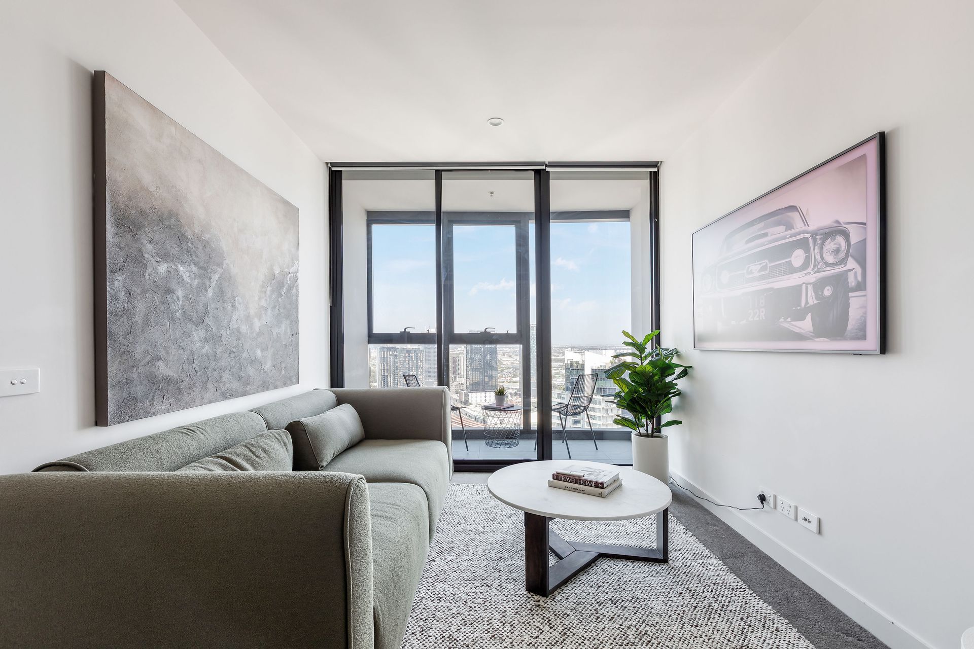 Modern living room with gray sofa, coffee table, large windows, and city view