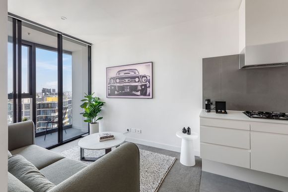 Modern apartment living room with gray sofa, balcony doors, city view, and compact kitchen area
