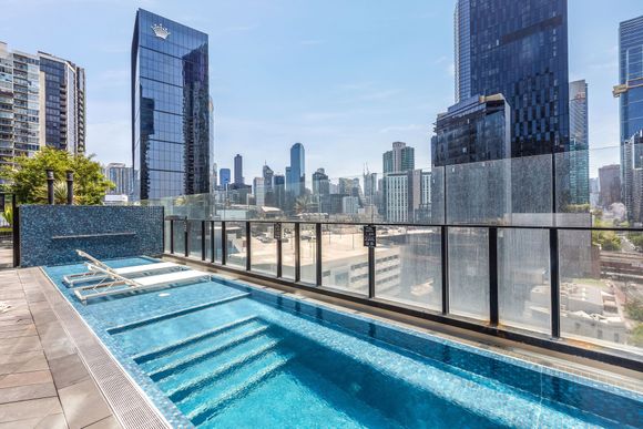 Rooftop pool with city skyline and glass railing under a clear blue sky