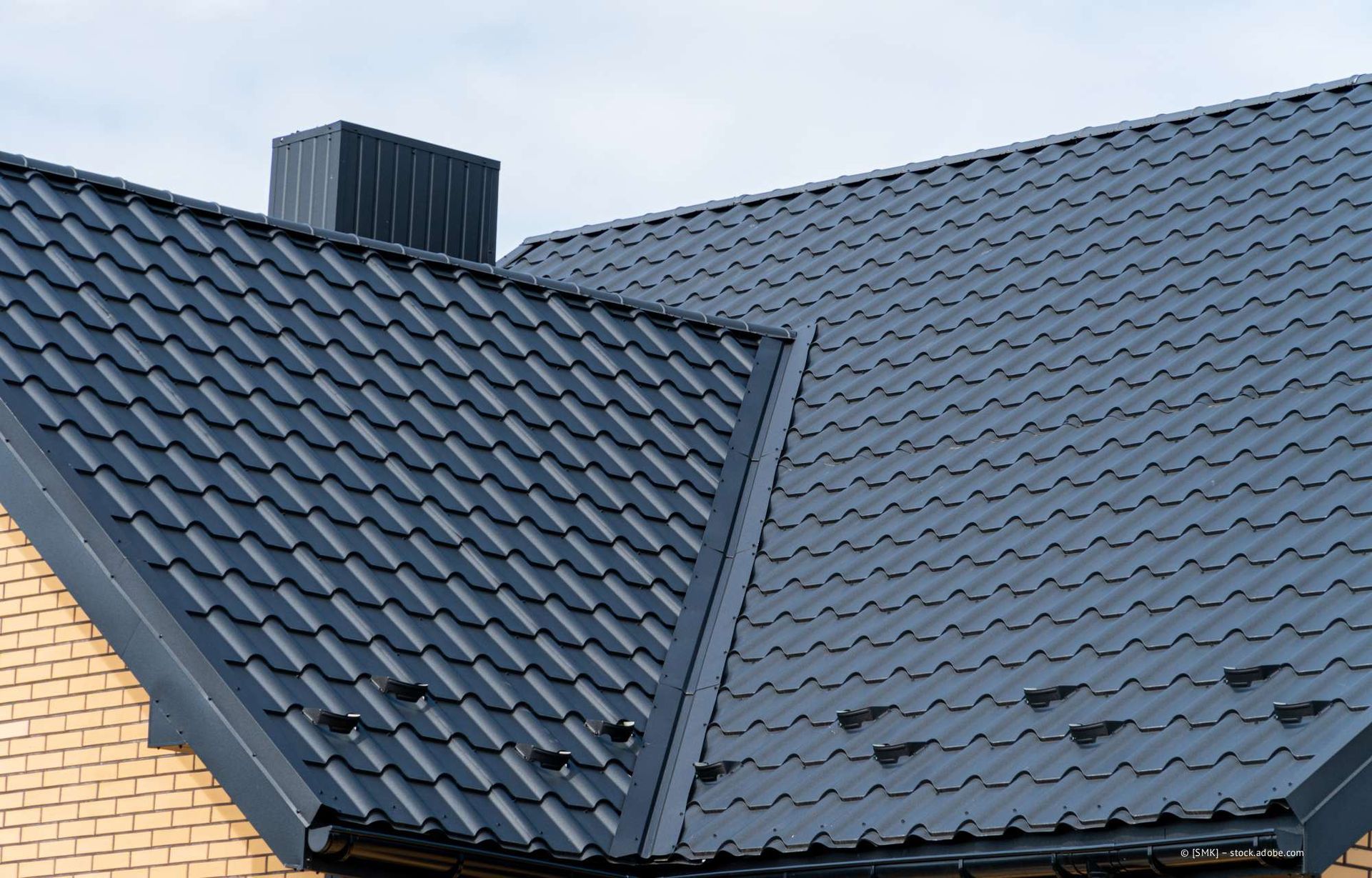 Dunkelgraues Metalldach auf einem Backsteingebäude mit schwarzem Schornstein.