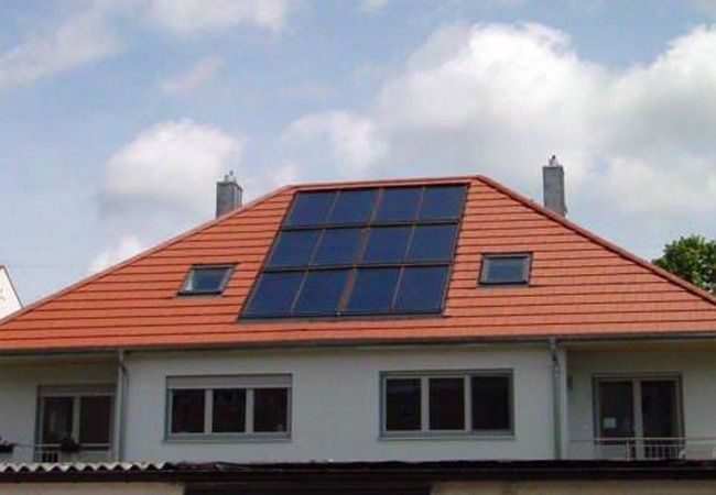 Solarpaneele auf dem roten Dach eines zweistöckigen weißen Gebäudes unter blauem Himmel.