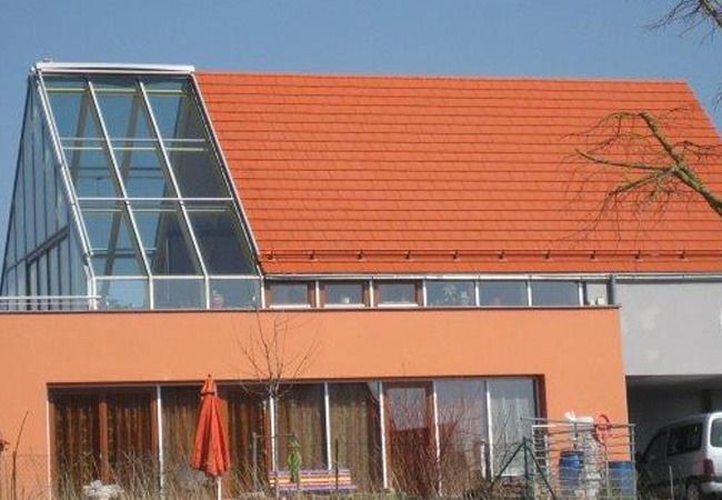 Orangefarbenes Haus mit verglastem Wintergarten, orangefarbenem Ziegeldach und klarem Himmel.