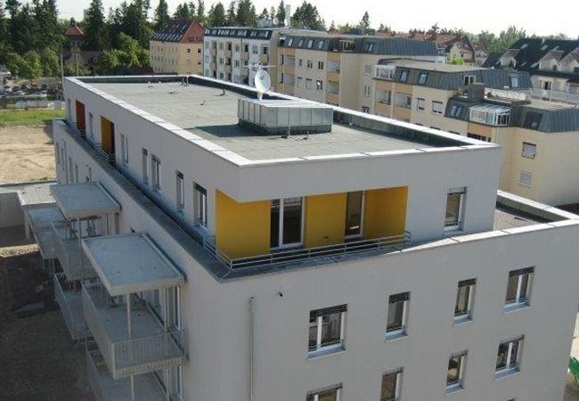 Mehrgeschossiges Wohnhaus mit Flachdach, Balkonen und gelben Akzenten.