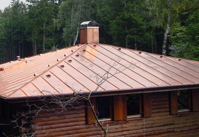 Kupferbedachung auf einer Blockhütte mit Schornstein. Das Dach ist von Bäumen umgeben.