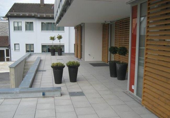 Außenansicht einer Gebäudeterrasse mit großen Pflanzkästen und Holzlamellen.