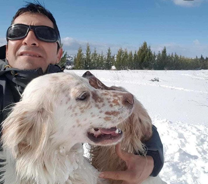 Un hombre con gafas de sol sostiene un perro blanco en un paisaje nevado bajo un cielo azul