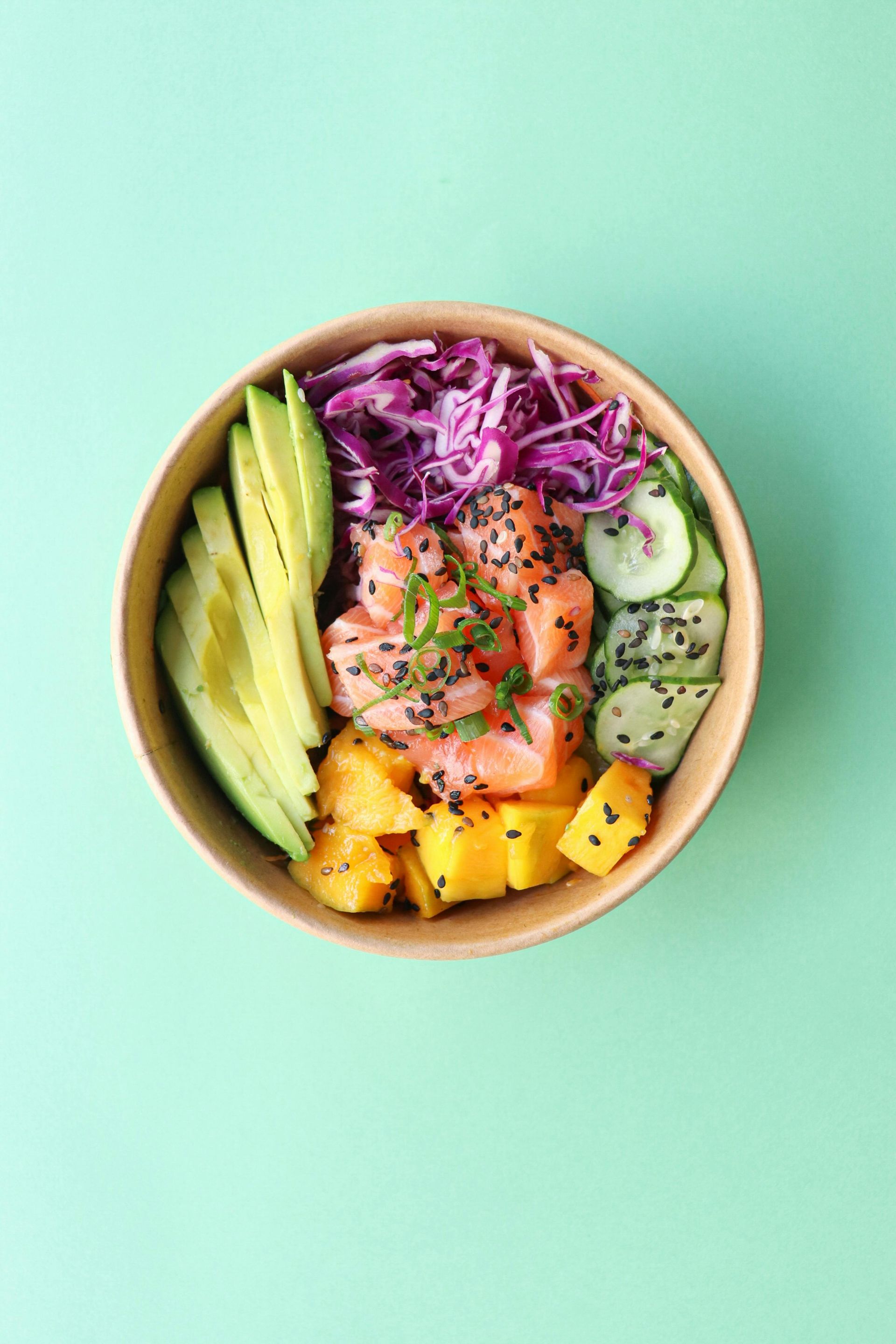 Un poke bowl con salmón, aguacate, pepino, repollo y mango sobre un fondo verde.