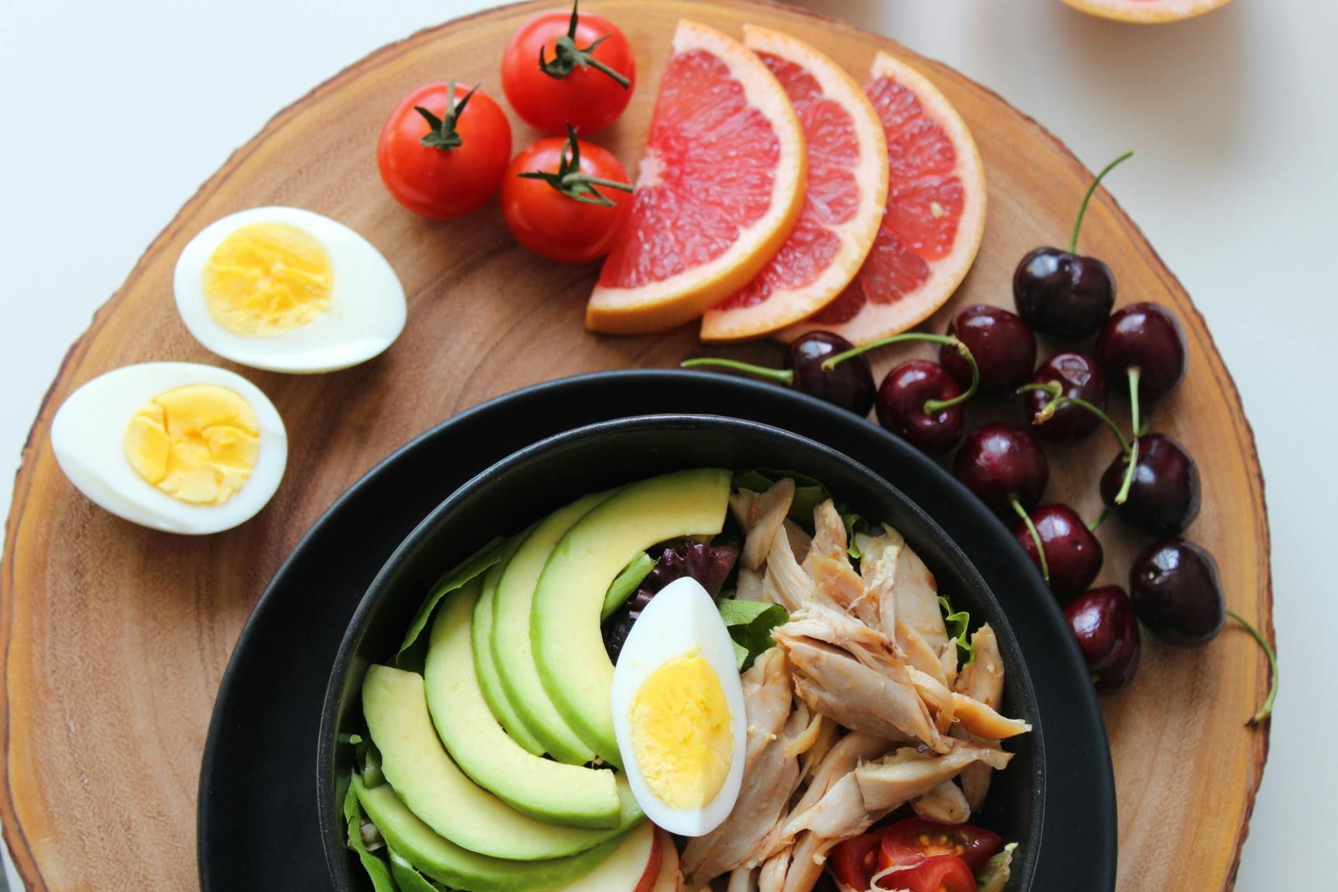 Ensalada saludable con aguacate, huevos y pollo. Decorada con tomate, pomelo y cerezas.