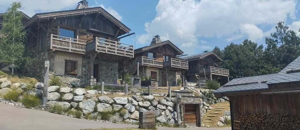 Casas de piedra en una ladera bajo un cielo azul, con balcones de madera y un sendero rocoso delante
