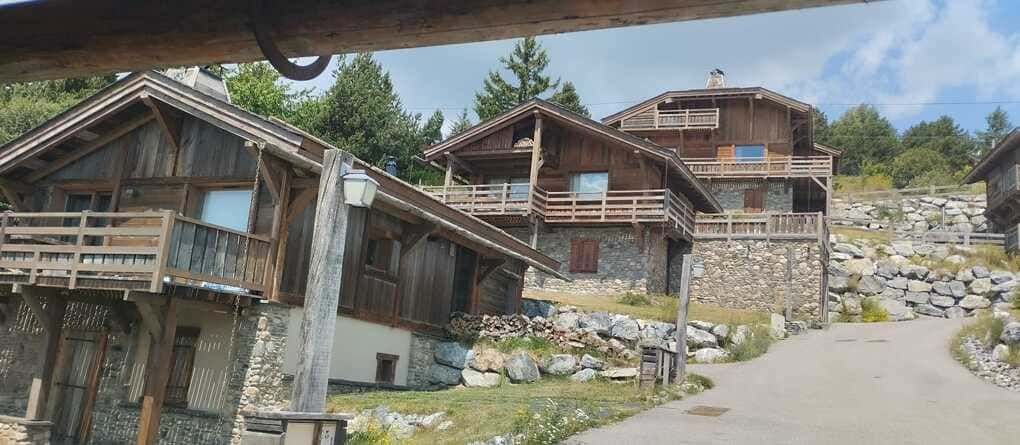 Pueblo rural en la ladera, con casas rústicas de madera, muros de piedra y una carretera estrecha bajo un cielo azul