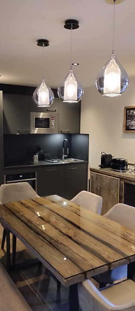 Cocina y comedor modernos con mesa de madera, lámparas colgantes y armarios oscuros