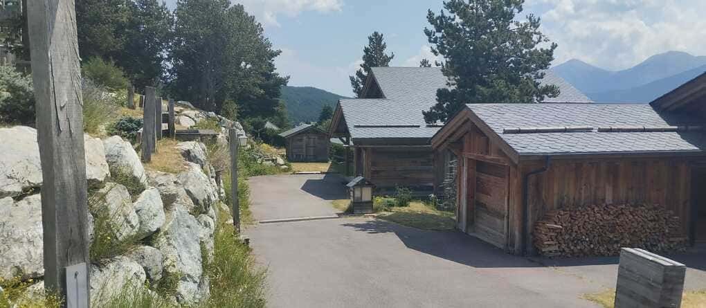 Camino de piedra entre cabañas rústicas de madera, con montañas y árboles al fondo