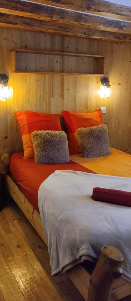 Acogedor dormitorio de madera con una cama doble vestida con ropa de cama naranja y blanca y lámparas de pared