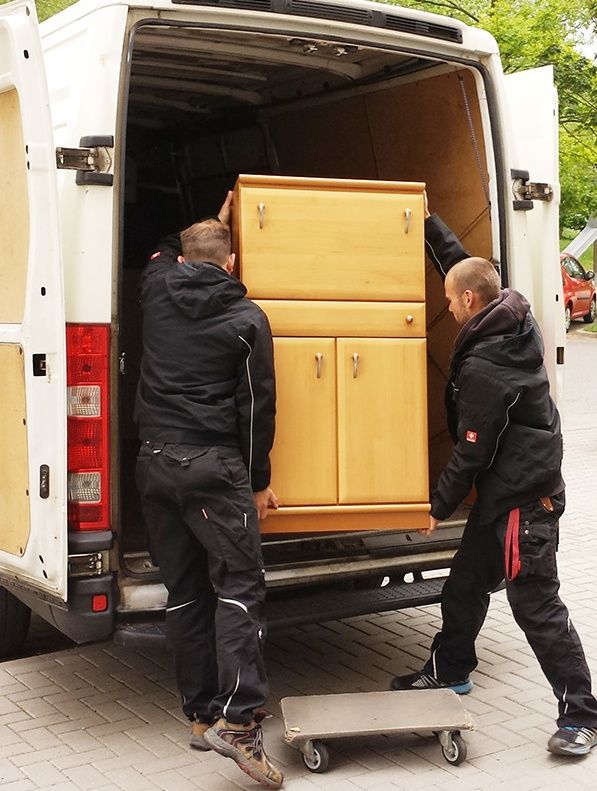 Zwei Mitarbeiter von Haushaltsberäumung Marcel Granz heben Kommode in einen Transporter