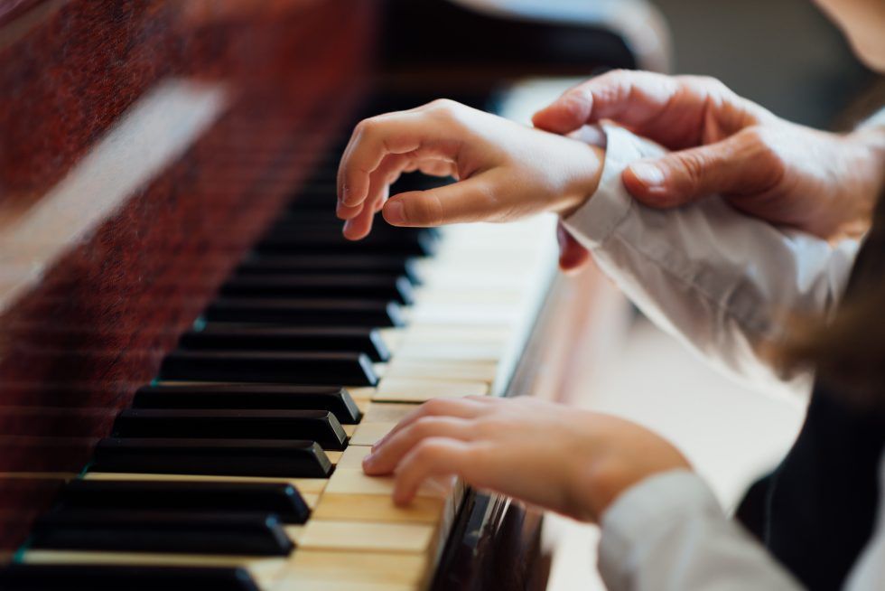 Una persona está enseñando a un niño a tocar el piano.
