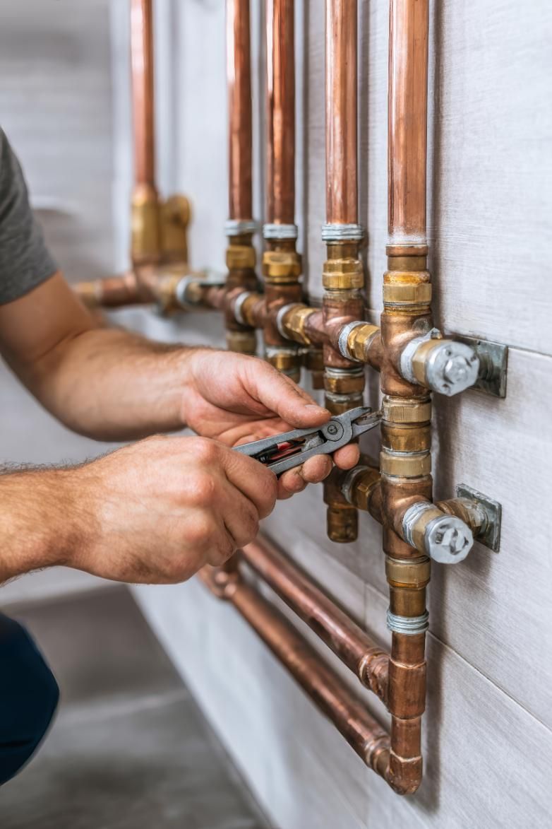 Fontanero utiliza una herramienta múltiple para ajustar tuberías y accesorios de cobre contra una pared blanca.