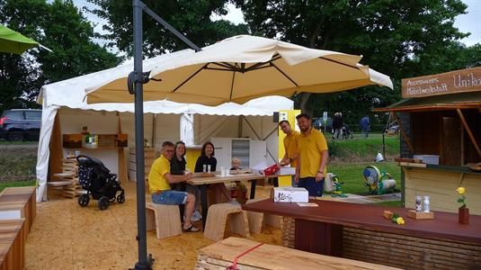 Eine Gruppe von Leuten sitzt an Tischen unter einem Sonnenschirm.