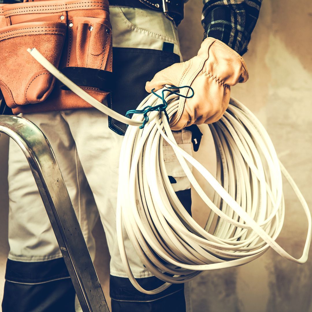 Persona con ropa de trabajo sosteniendo una bobina de alambre blanco y usando guantes de trabajo de cuero.