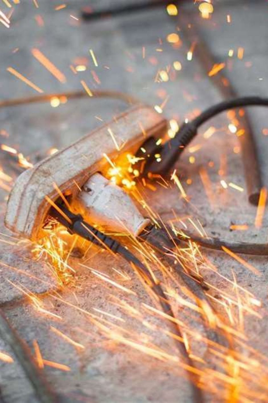 Saltan chispas de un tomacorriente eléctrico con un cable enchufado, sobre una superficie de baldosas.