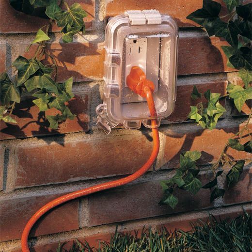 Cubierta de toma de corriente transparente resistente a la intemperie sobre una pared de ladrillos.