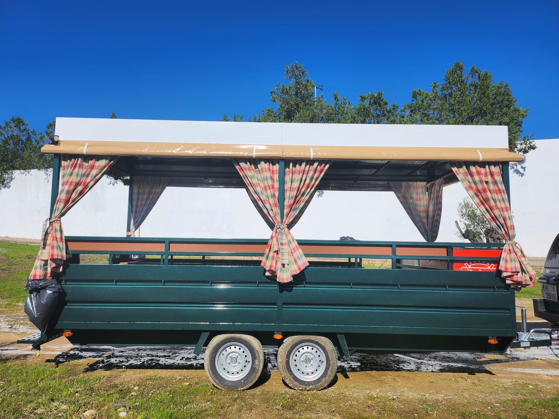 Remolque verde con techo color canela, cortinas a cuadros rojos y canela y ruedas dobles.