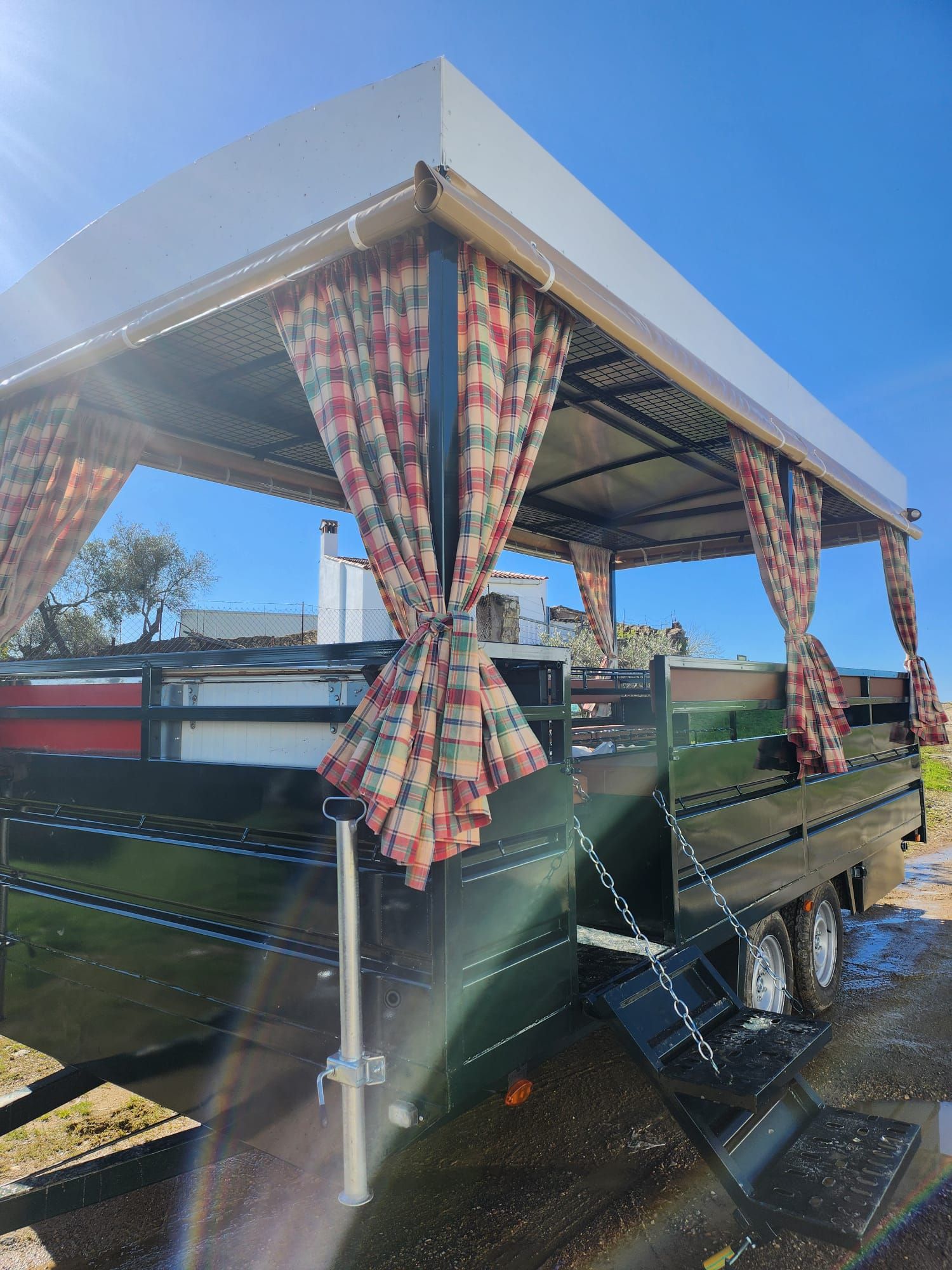 Remolque verde con toldo y cortinas estampadas, bajo un cielo azul brillante.