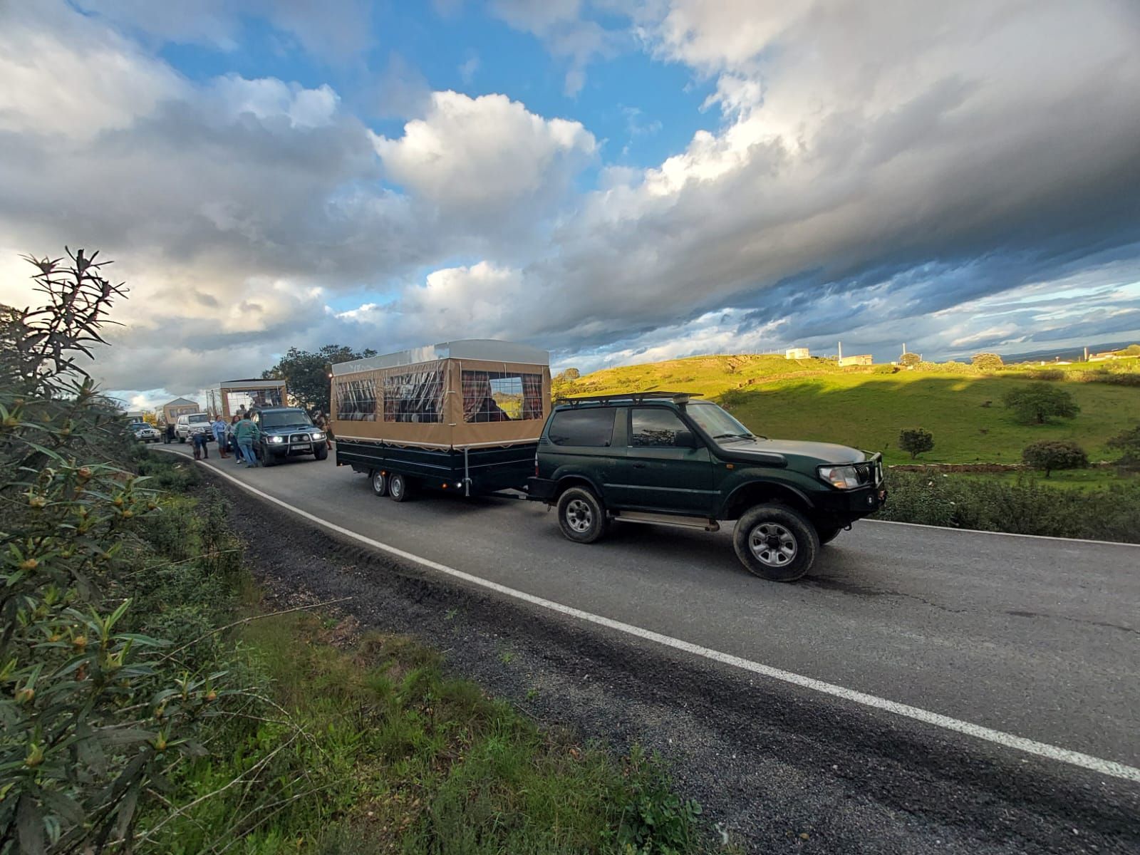 Una camioneta verde arrastraba un remolque con estructura cubierta por la carretera. Cielo nublado.