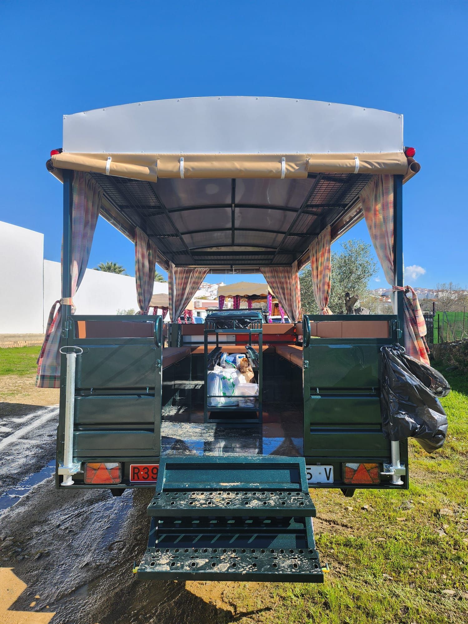 Vista trasera de un carrito de comida móvil con mostradores, parrilla y escalones. Exterior verde oscuro y blanco.