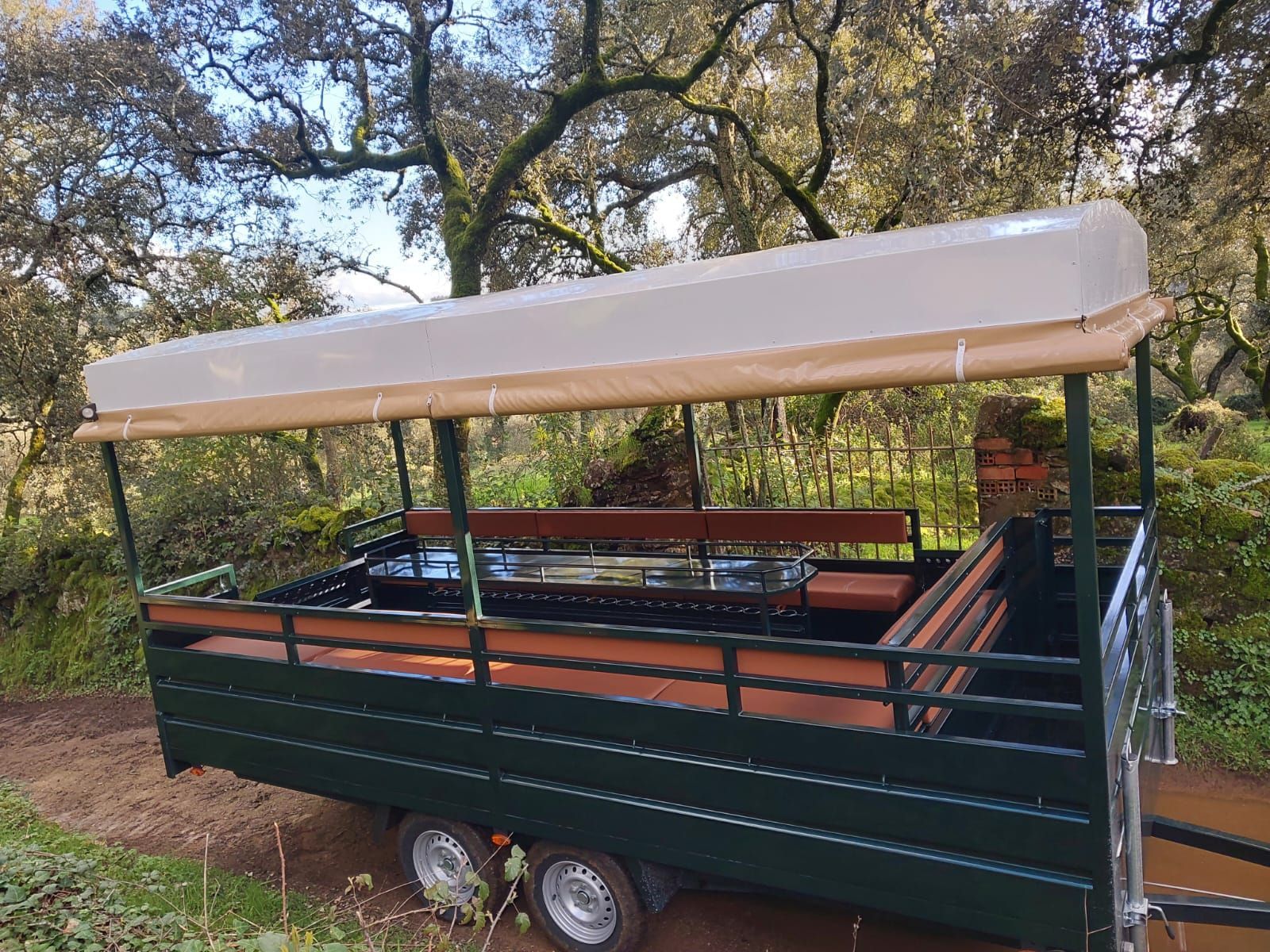 Remolque verde con toldo color canela y bancos de madera, en zona boscosa.