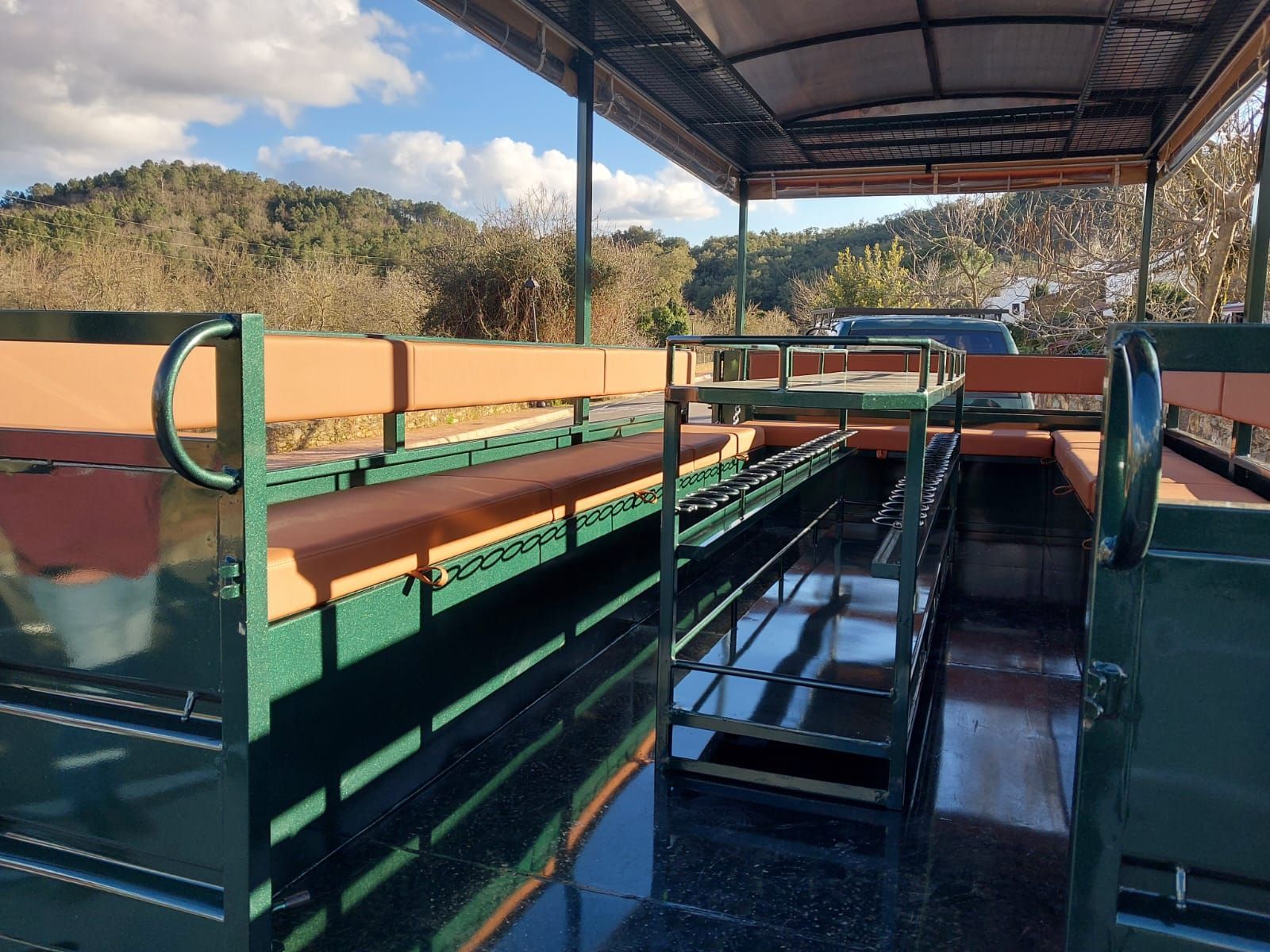 Interior de un vehículo de safari al aire libre. Estructura metálica verde con asientos marrones, con vistas a la naturaleza.