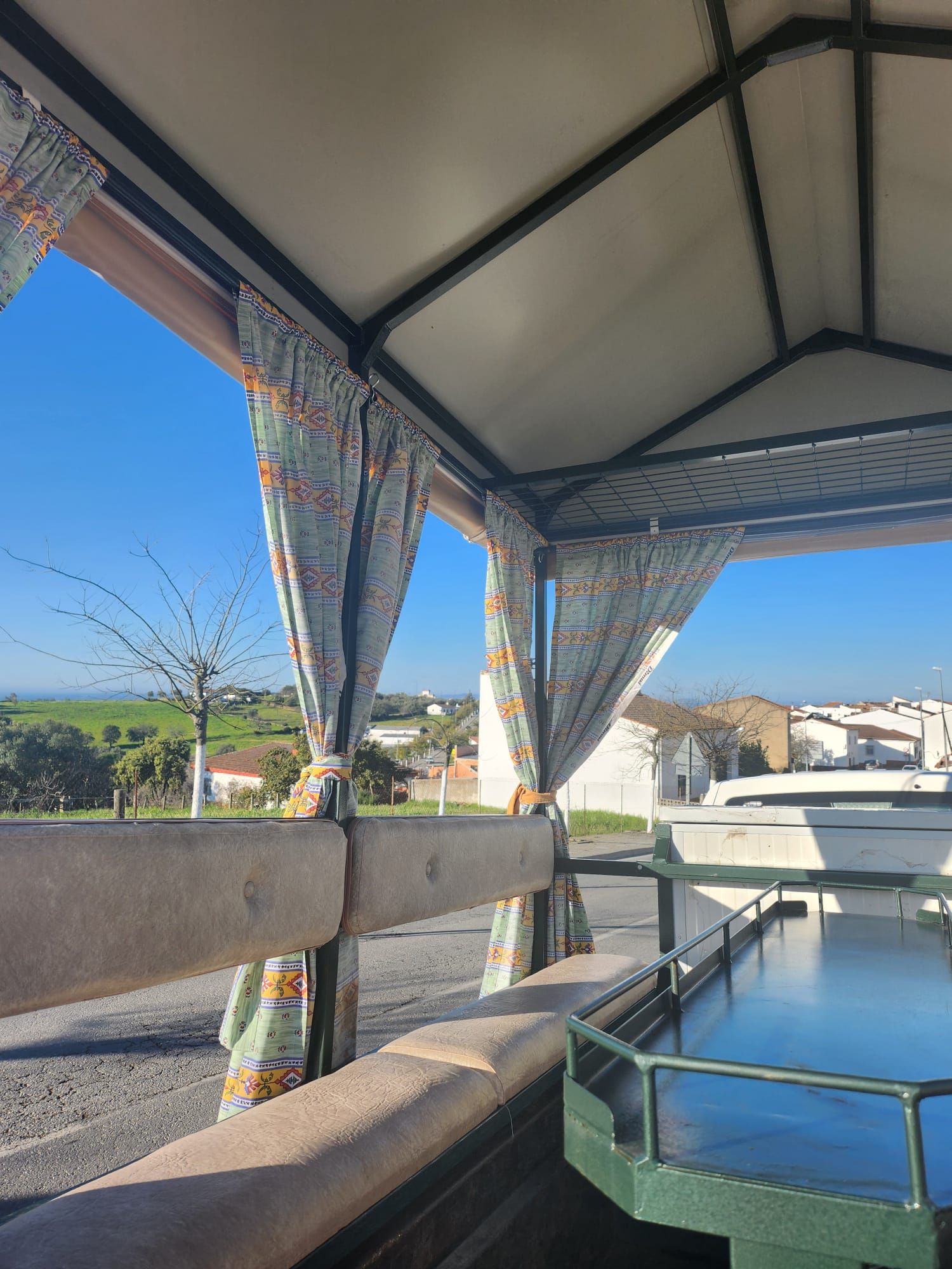 Cenador con cortinas estampadas con vista a un paisaje verde brillante y casas bajo un cielo azul claro.
