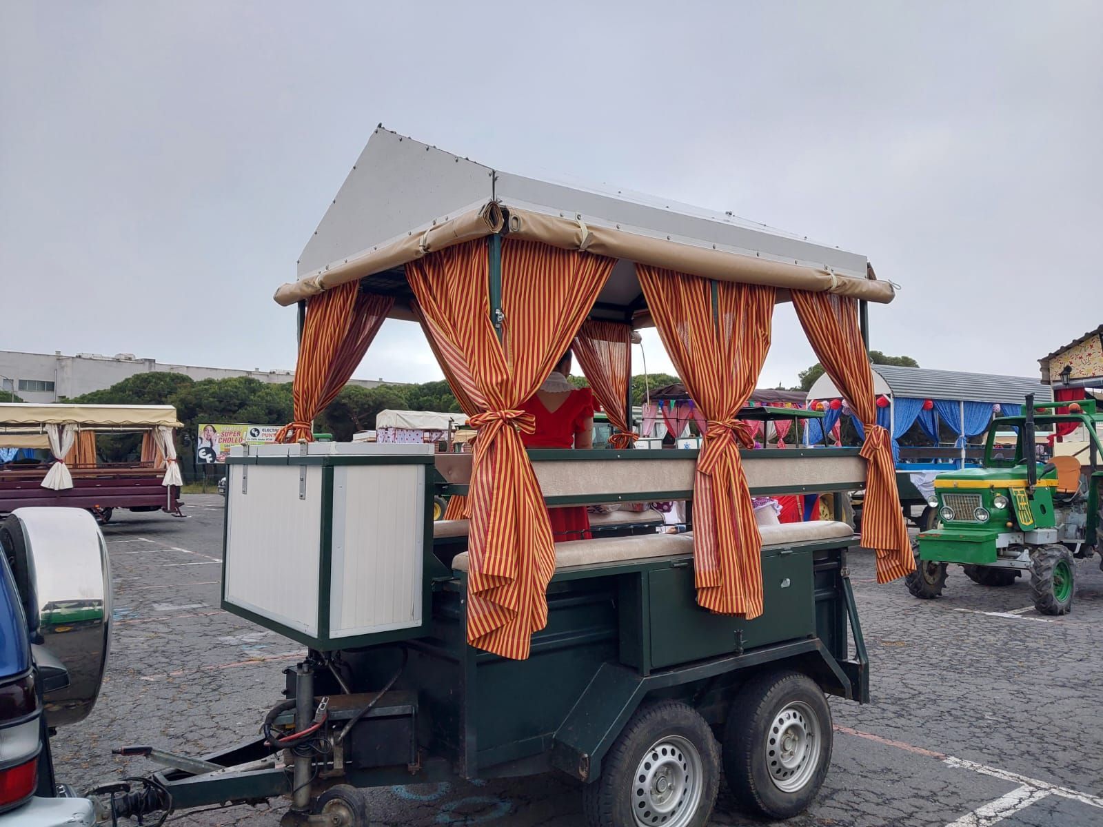 Un carrito de comida con un techo de cortina de rayas naranjas y cortinas laterales se encuentra afuera en un lote pavimentado.