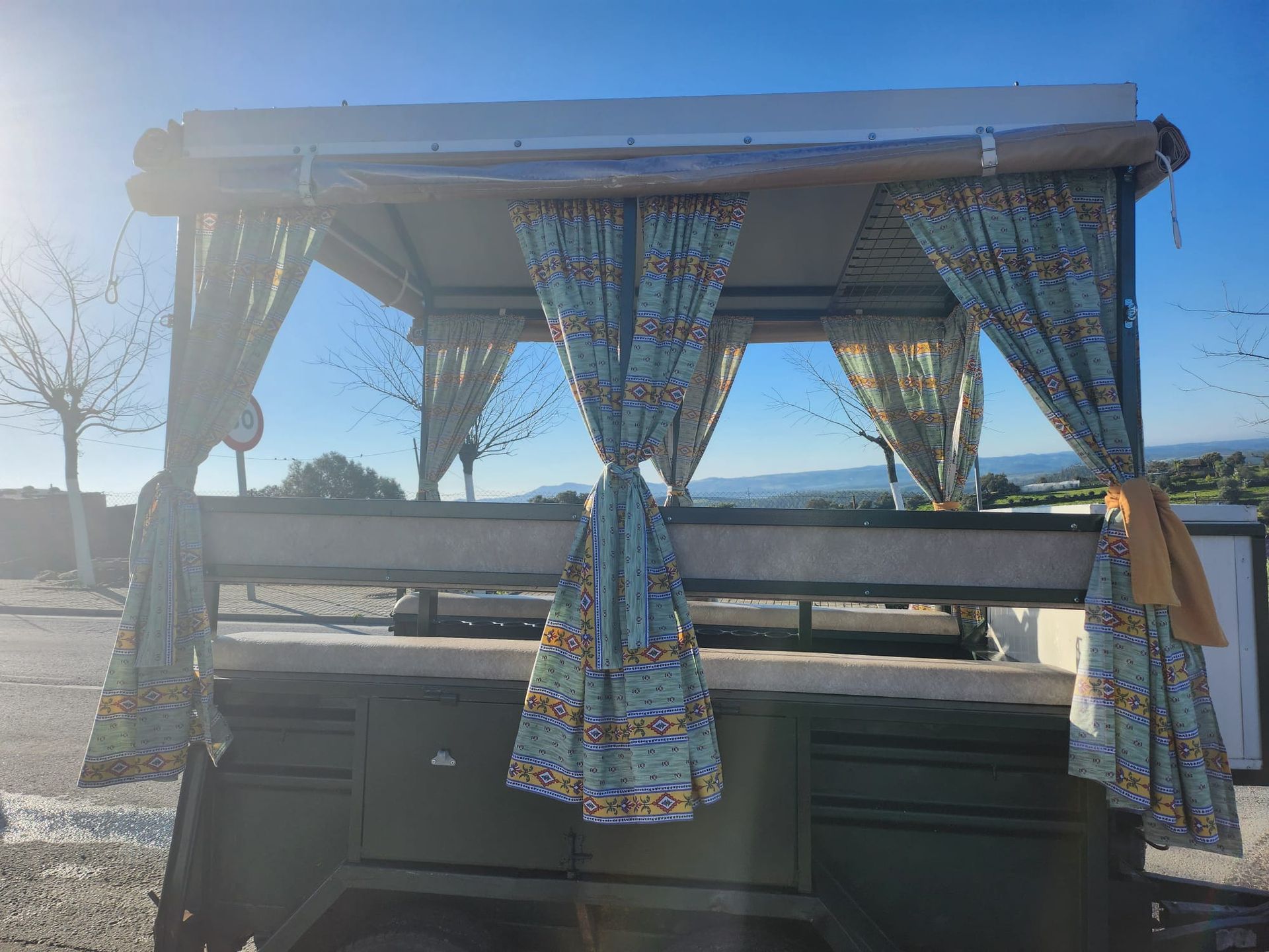 Remolque verde con cortinas con estampados azules, toldo y fondo rural.