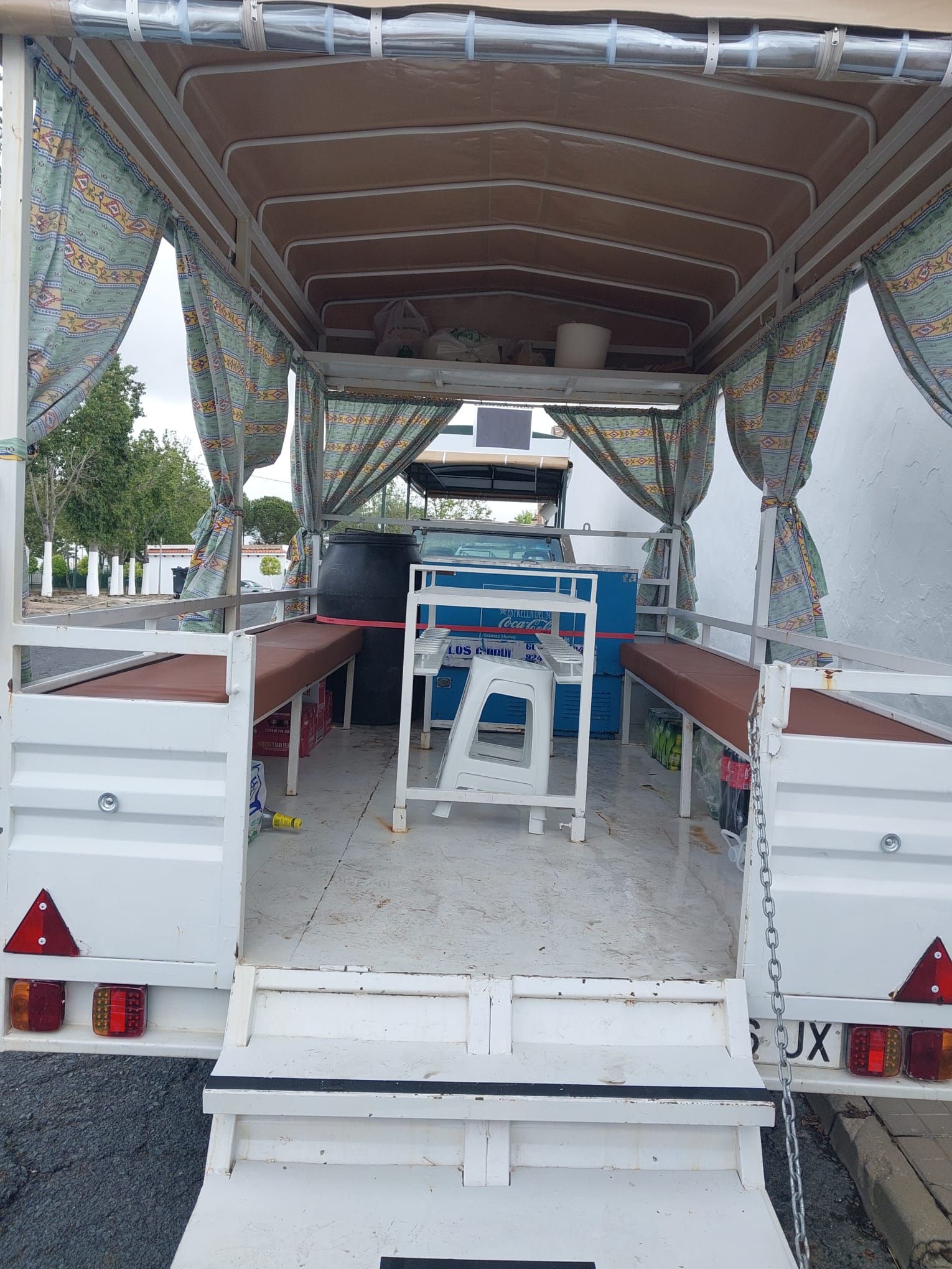 Interior de remolque blanco abierto, con bancos laterales y mesa central, cortinas y toldo superior.