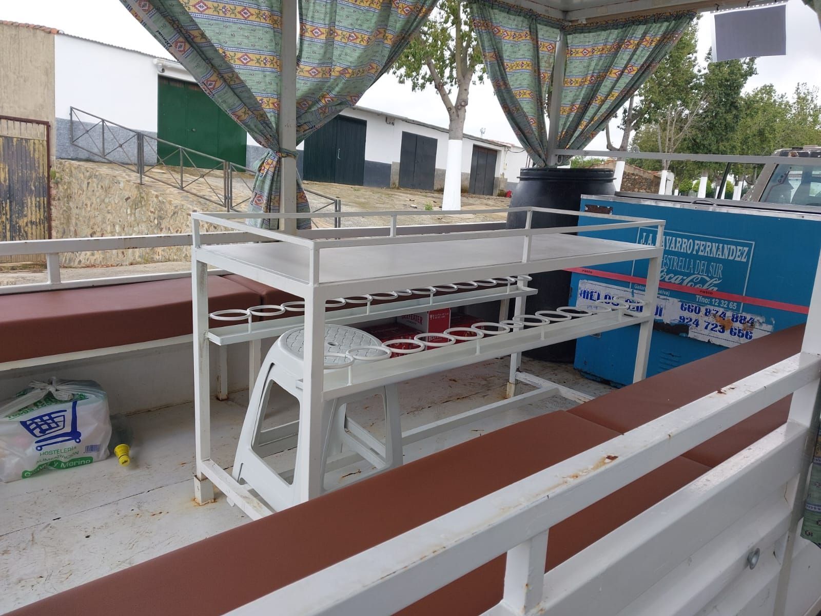 Una estantería de metal blanco que contiene contenedores rojos y negros, en un barco con bancos marrones.