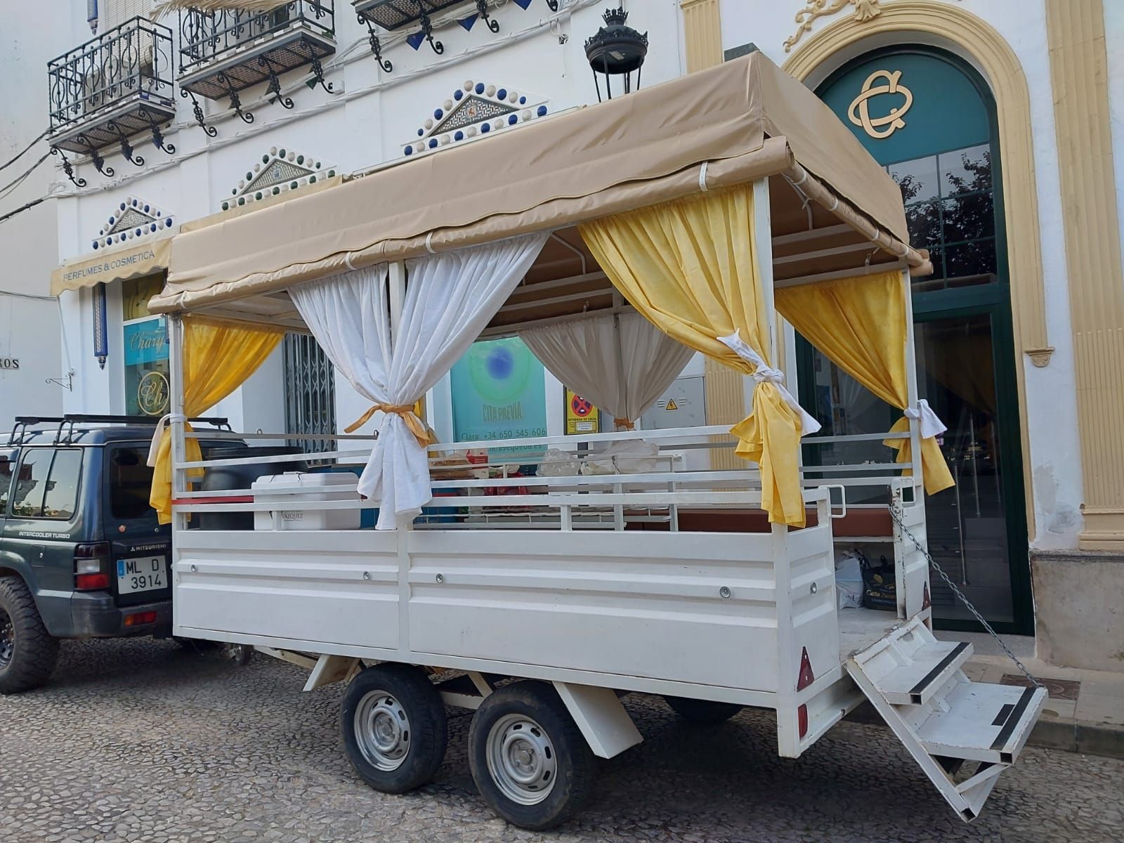 Un remolque decorado con un toldo color canela y cortinas amarillas y blancas, estacionado afuera de un edificio.