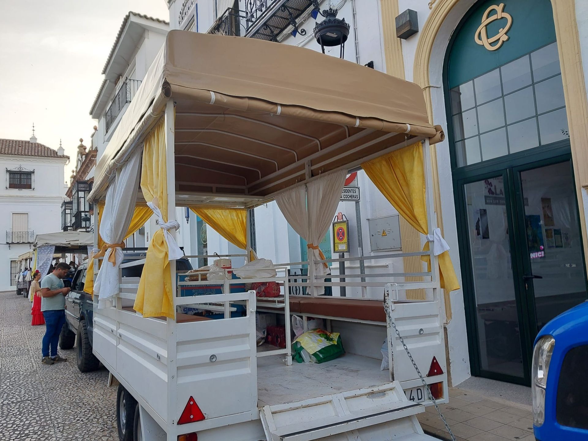 Remolque blanco con toldo color tostado y cortinas amarillas estacionado afuera de un edificio con una puerta verde.