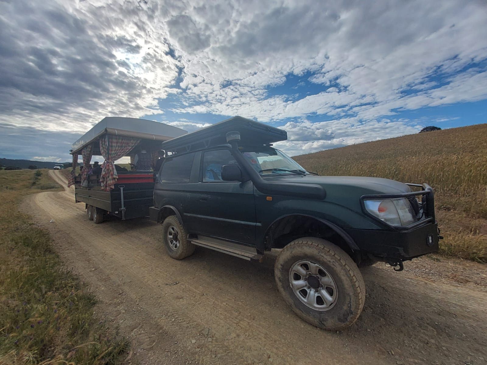Un todoterreno verde oscuro remolca una caravana por un camino de tierra bajo un cielo nublado.