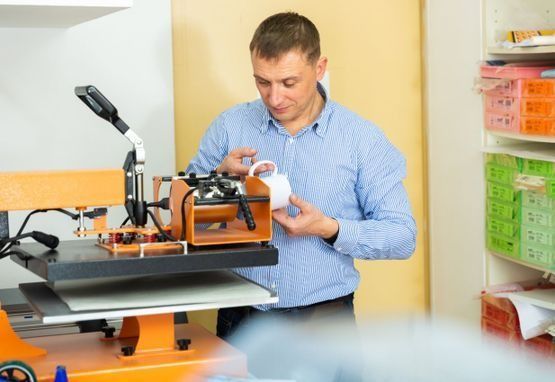 Hombre que utiliza una máquina de prensado térmico para imprimir en una taza en un taller.