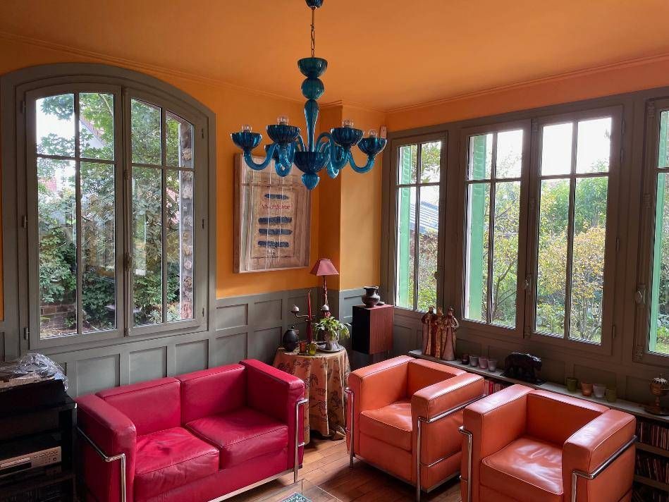 Chambre orange avec des meubles rouges et orange, de grandes fenêtres et un lustre bleu.
