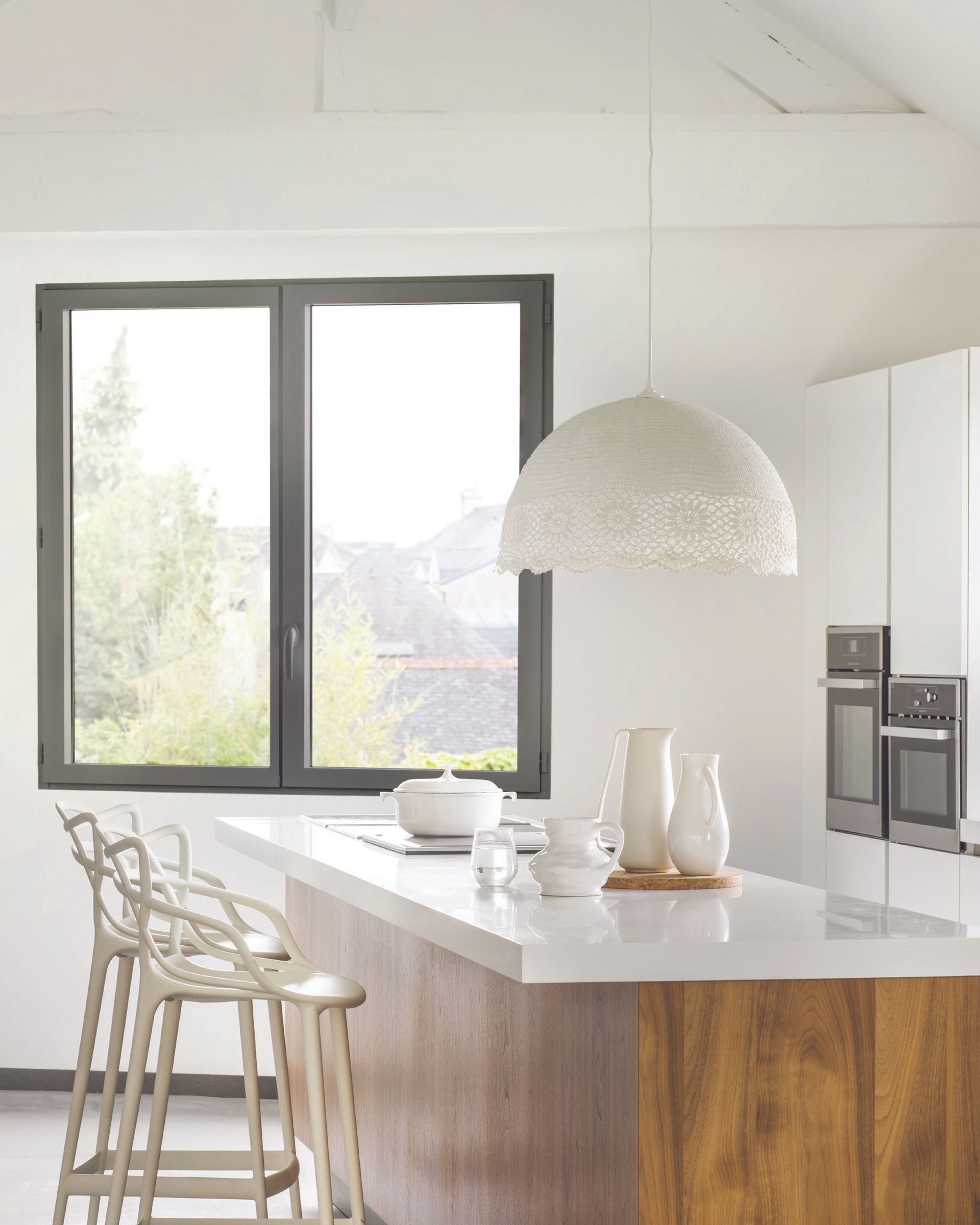 Cuisine blanche avec îlot en bois, fenêtre, suspension lumineuse et tabourets de bar.