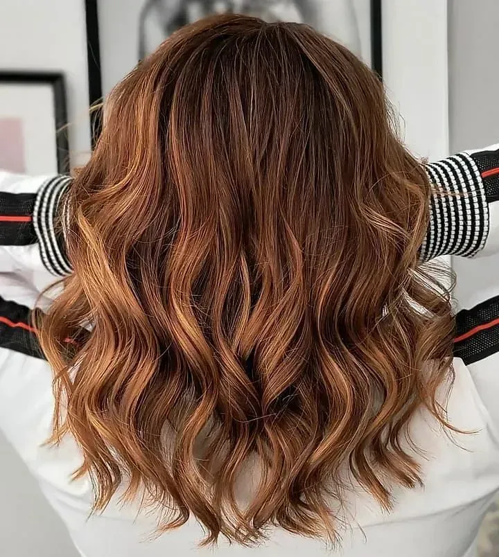 La parte posterior de la cabeza de una mujer con cabello castaño largo y ondulado.