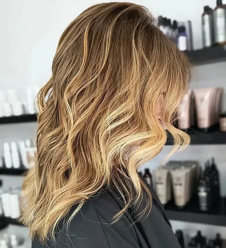 Una mujer con cabello largo y rubio está parada frente a un estante de productos para el cabello.
