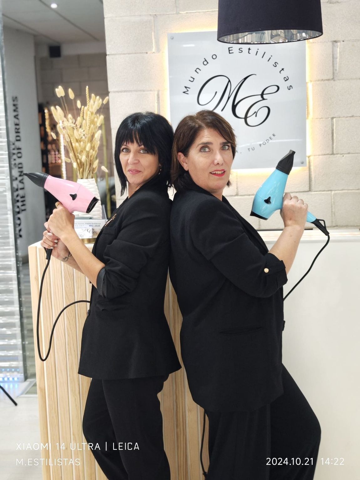 Dos mujeres paradas una al lado de la otra sosteniendo secadores de pelo