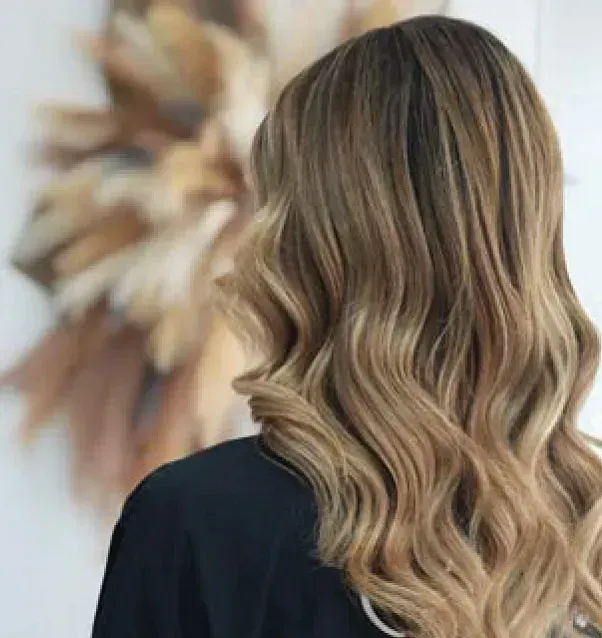 Una mujer con cabello rubio largo y ondulado está parada frente a una corona de flores.