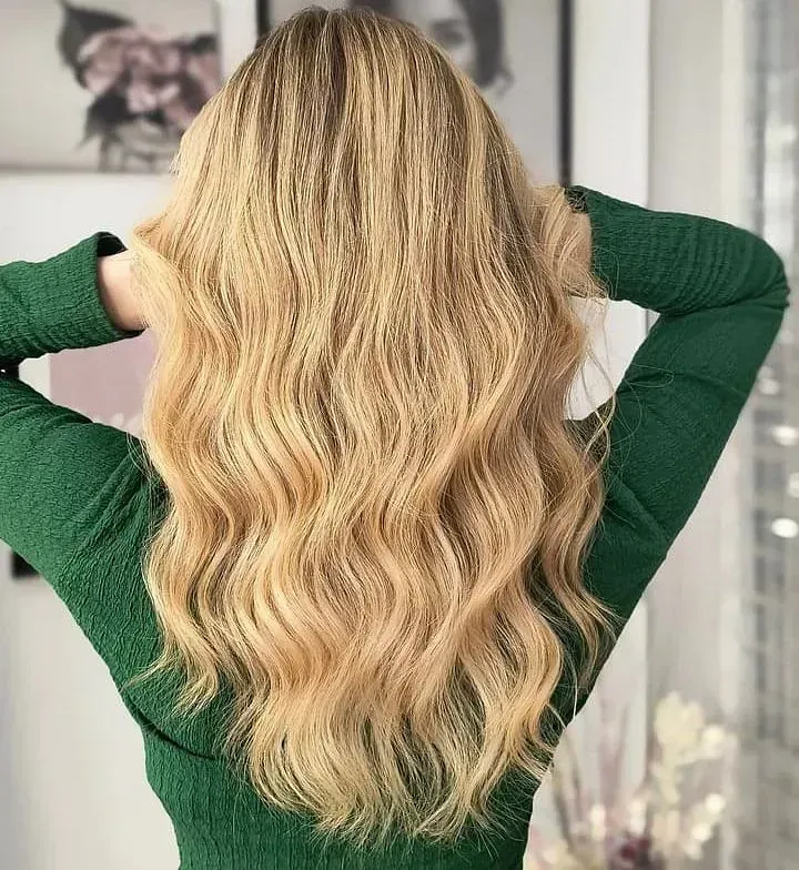 Una mujer con cabello largo y rubio lleva un suéter verde.