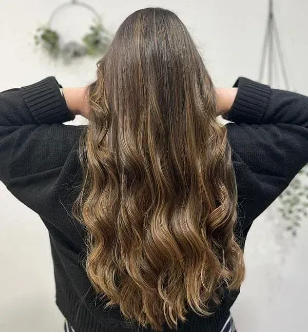 Una mujer con cabello largo y castaño lleva un suéter negro.